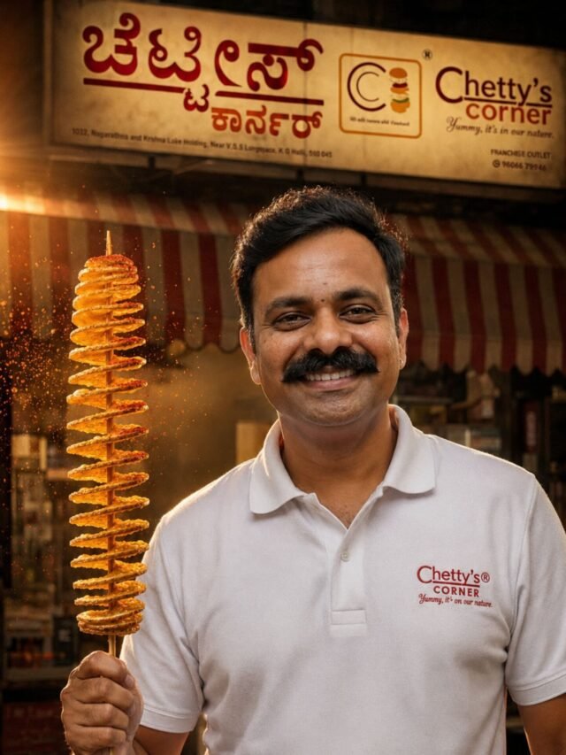 Smiling Anil Chetty wearing a Chetty's Corner branded polo shirt, holding the original crispy Twistato spiral potato in front of the Chetty's Corner outlet.